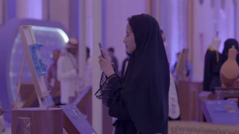 A woman is photographing a model of a startup project in the hall of the Global Entrepreneurship Conference from December 21 to 23, 2025, at the King Abdulaziz International Conference Center in Riyadh, Saudi Arabia's support for startups, discussing innovation and modern technology.