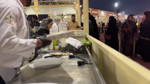 اعداد وطهي الفطائر والبيتزا في مهرجان إثراء للطعام من ٢٢ ديسمبر حتى ع يناير ٢٠٢٦، مركز الملك عبد العزيز للثقافة العالمية (إثراء) في الظهران في المملكة العربية السعودية، تصميم فريد يشبه الحصى، يضم مرافق ثقافية وتعليمية متنوعة مثل مكتبة ومتحف ومسرح وسينما