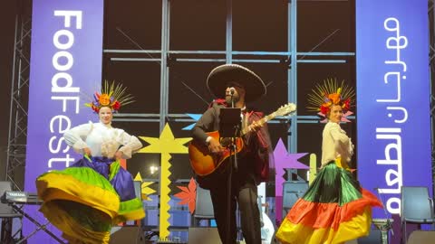 المغني في المنتصف ويعزف على الجيتار، رقصة فولكلورية مكسيكية، مهرجان إثراء للطعام من ٢٢ ديسمبر حتى ع يناير ٢٠٢٦، مركز الملك عبد العزيز للثقافة العالمية (إثراء) في الظهران في المملكة العربية السعودية، تصميم فريد يشبه الحصى