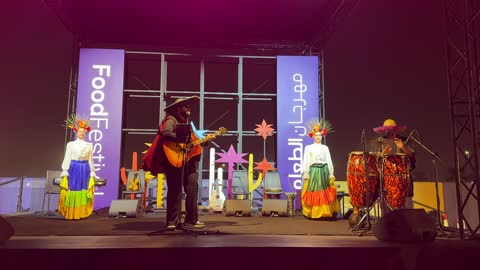 رجل في منتصف المسرح ترقص امرأتان بفساتين واسعة، مهرجان إثراء للطعام من ٢٢ ديسمبر حتى ع يناير ٢٠٢٦، رقصة فولكلورية مكسيكية، مركز الملك عبد العزيز للثقافة العالمية (إثراء) في الظهران في المملكة العربية السعودية، تصميم فريد يشبه الحصى