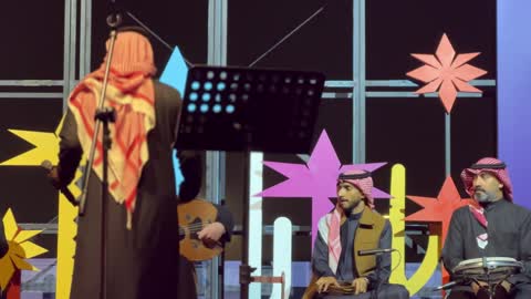 مغني يؤدي عرض حي على خشبة المسرح محاط بموسيقيين، فرقة موسيقية تقليدية على خشبة مسرح مضاءة، مهرجان إثراء للطعام من ٢٢ ديسمبر حتى ع يناير ٢٠٢٦، مركز الملك عبد العزيز للثقافة العالمية (إثراء) في الظهران في المملكة العربية السعودية، تصميم فريد يشبه الحصى
