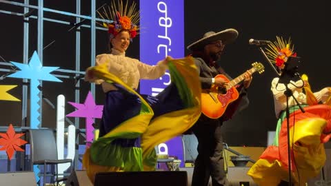 لافتات الموجودة المسرح نص باللغتين الإنجليزية والعربية ، رقصة فولكلورية مكسيكية، مهرجان إثراء للطعام من ٢٢ ديسمبر حتى ع يناير ٢٠٢٦، مركز الملك عبد العزيز للثقافة العالمية (إثراء) في الظهران في المملكة العربية السعودية، تصميم فريد يشبه الحصى