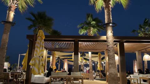 The use of heaters in outdoor seating, the sea breeze at the Corniche of Khobar in the Eastern Province, Kingdom of Saudi Arabia, entertainment events and activities, tourist restaurants and cafes, a family-friendly coastal beach destination, a calm atmosphere, and an enjoyable relaxation experience.