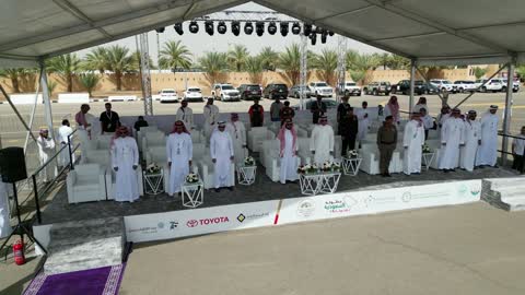 Fans wearing traditional Saudi attire, the championship and sports activities in the city of Tabuk, the rally race event in the Kingdom of Saudi Arabia, the speed race for cars, the competition and rivalry to achieve victory, the turns and directions for the competing cars.