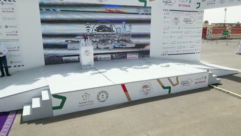 Delivering a speech and announcing the start of the race, the championship and sports activities in the city of Tabuk, the rally race event in the Kingdom of Saudi Arabia, the speed race for cars, the competition and rivalry to achieve victory, the turns and directions for the competing cars.