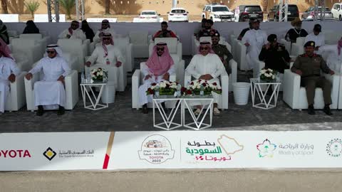 Fans wearing traditional Saudi attire, the championship and sports activities in the city of Tabuk, the rally race event in the Kingdom of Saudi Arabia, the speed race for cars, the competition and rivalry to achieve victory, the turns and directions for the competing cars.