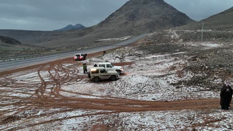 رحلة سفاري وتخييم في منطقة باردة، سلسلة جبال الحرة في منطقة تبوك تكسوها الثلوج، أجواء ثلجية باردة، جبال منحوتة وتشكيلات جبلية في مدينة تبوك، معالم حضارية سياحية في المملكة العربية السعودية، تصوير درون جوي للتكوينات الصخرية