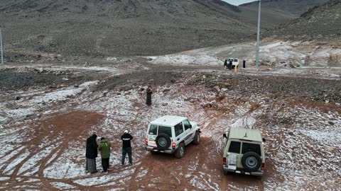 A safari and camping trip in a cold area, the Al-Harra mountain range in the Tabuk region covered in snow, cold snowy atmosphere, sculpted mountains and geological formations in the city of Tabuk, cultural and tourist landmarks in the Kingdom of Saudi Arabia, aerial drone photography of rock formations.