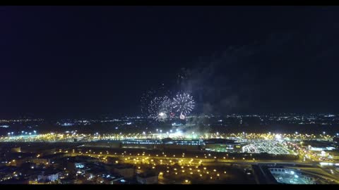 Celebration and joy manifestations, drone footage of fireworks and firecrackers in the sky of Tabuk city at night, traffic movement of cars in the city's streets.