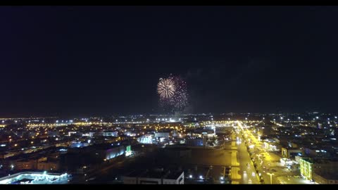 Celebration and joy manifestations, drone footage of fireworks and firecrackers in the sky of Tabuk city at night, traffic movement of cars in the city's streets.