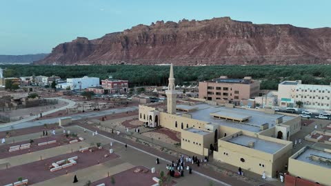 A place for worship and getting closer to God Almighty, a drone shot of an Islamic mosque in Al-Ula Governorate in the Kingdom of Saudi Arabia, trees and green plants, mountains and rock formations, a famous tourist area.