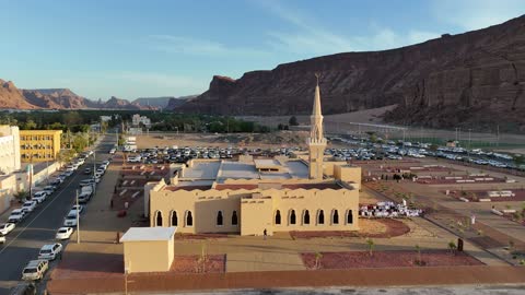 A place for worship and getting closer to God Almighty, a drone shot of an Islamic mosque in Al-Ula Governorate in the Kingdom of Saudi Arabia, trees and green plants, mountains and rock formations, a famous tourist area.