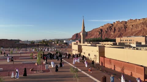 A place for worship and getting closer to God Almighty, a drone shot of an Islamic mosque in Al-Ula Governorate in the Kingdom of Saudi Arabia, trees and green plants, mountains and rock formations, a famous tourist area.