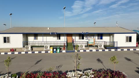 غرفة الإدارة في مصنع متخصص في أعمال الخرسانة الجاهزة والأساسات الميكانيكية ، خلط مكونات الخرسانة ، عجينة اسمنتية للبناء والانشاء ، اماكن انشائية، أكوام كبيرة من المواد الخام الحصى، نباتات خضراء وزهور في منصف الطريق