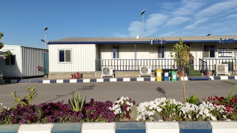 غرفة الإدارة في مصنع متخصص في أعمال الخرسانة الجاهزة والأساسات الميكانيكية ، خلط مكونات الخرسانة ، عجينة اسمنتية للبناء والانشاء ، اماكن انشائية، أكوام كبيرة من المواد الخام الحصى، نباتات خضراء وزهور في منصف الطريق