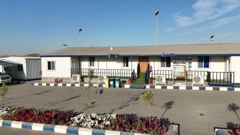 A ready-made white exterior building with a blue roof, a factory specialized in ready-mix concrete works and mechanical foundations, mixing concrete components, cement paste for construction and establishment, construction sites, large piles of raw materials such as gravel, sand, or aggregates stored under structures.