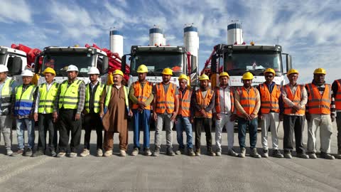 عمال إنشاءات يقفون أمام شاحنات خلط خرسانة، مركبات لنقل الخرسانة الجاهزة من المصنع إلى مواقع البناء، إنتاج الخرسانة لمشاريع البناء والهندسة المدنية ، مصنع متخصص في أعمال الخرسانة الجاهزة والأساسات الميكانيكية ، خلط مكونات الخرسانة ، عجينة اسمنتية للبناء والانشاء