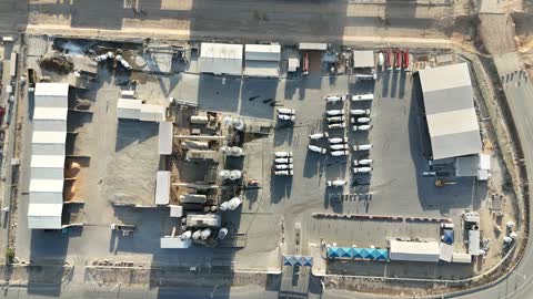 A factory specialized in ready-mixed concrete works and mechanical foundations, mixing concrete components, cement paste for construction and building, construction sites, large piles of raw materials such as gravel, sand, or aggregates stored under structures, concrete barriers to separate stored materials.