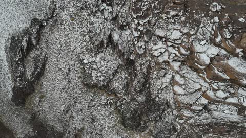 High-altitude desert areas, tourist cultural landmarks in the Kingdom of Saudi Arabia, cold snowy atmospheres, the Al-Harra mountain range in the Tabuk region covered in snow, sculpted mountains and geological formations, aerial drone photography of rock formations.