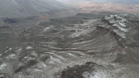 Light accumulation of snow on the peaks and rocky elevations, cultural and tourist landmarks in the Kingdom of Saudi Arabia, cold snowy atmosphere, the Al-Harra mountain range in the Tabuk region covered in snow, sculpted mountains and geological formations, aerial drone photography of the rock formations.