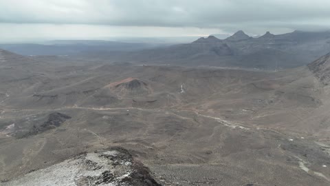 High-altitude desert areas, tourist cultural landmarks in the Kingdom of Saudi Arabia, cold snowy atmospheres, the Al-Harra mountain range in the Tabuk region covered in snow, sculpted mountains and geological formations, aerial drone photography of rock formations.