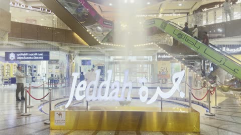 مجسم مضاء باسم جدة Jeddah فى مركز المحمل التجاري في منطقة البلد التاريخية بمدينة جدة، المملكة العربية السعودية، معلم تجاري وتراثي بارز، متاجر متنوعة للذهب والملابس والعطور، وجهة تسوق تعكس الطابع التاريخي للمنطقة، موقع حيوي بالقرب من الأسواق التقليدية والمعالم التاريخية.