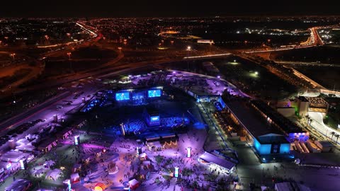 A green flag fluttering on a pole, the famous roads, streets, and landmarks of Jeddah, drone footage of a road in the city of Jeddah in the Kingdom of Saudi Arabia at night, car traffic, towers and residential buildings, a large number of people in the area.