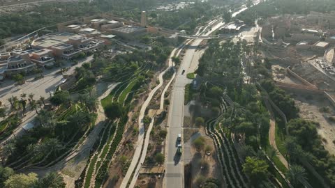 A path surrounded by green spaces, a center and a famous historical cultural and tourist landmark in Saudi Arabia at night, the illuminated Al-Bujairi Park and overlook during the day, the development project of historical Diriyah in the city of Riyadh, Saudi Arabia, the heritage village and archaeological buildings.