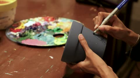 Mastering the art of handicrafts, spending free time on something useful, a close-up shot of a woman painting and decorating a ceramic flower pot.