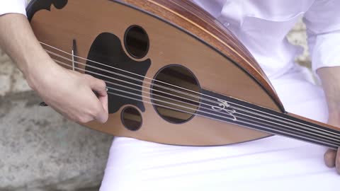 اتقان فن العزف الموسيقي، تصوير مقرب لعازف عربي خليجي سعودي محترف يجلس ويعزف على آلة العود