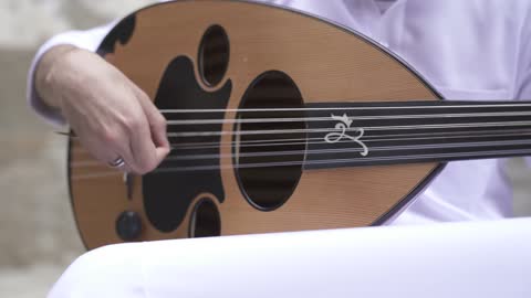 اتقان فن العزف الموسيقي، تصوير مقرب لعازف عربي خليجي سعودي محترف يجلس ويعزف على آلة العود