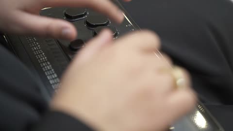 Providing devices that assist people with disabilities, a close-up shot of a Saudi Gulf Arab woman wearing a black abaya who is blind and is reading using an electronic Braille device.