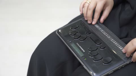 توفير اجهزة تساعد ذوي الهمم، تصوير مقرب لامرأة عربية خليجية سعودية ترتدي عباءة سوداء كفيفة تقوم بالقراءة باستخدام جهاز برايل الإلكتروني