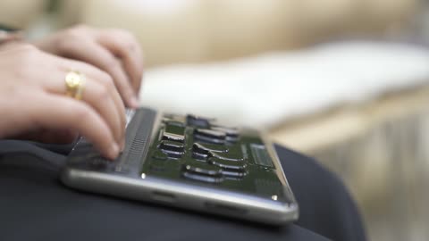 Providing devices that assist people with disabilities, a close-up shot of a Saudi Gulf Arab woman wearing a black abaya who is blind and is reading using an electronic Braille device.
