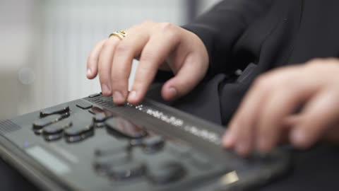 توفير اجهزة تساعد ذوي الهمم، تصوير مقرب لامرأة عربية خليجية سعودية ترتدي عباءة سوداء كفيفة تقوم بالقراءة باستخدام جهاز برايل الإلكتروني