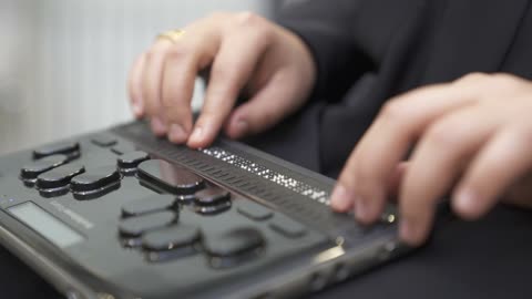 توفير اجهزة تساعد ذوي الهمم، تصوير مقرب لامرأة عربية خليجية سعودية ترتدي عباءة سوداء كفيفة تقوم بالقراءة باستخدام جهاز برايل الإلكتروني