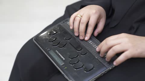 Providing devices that assist people with disabilities, a close-up shot of a Saudi Gulf Arab woman wearing a black abaya who is blind and is reading using an electronic Braille device.