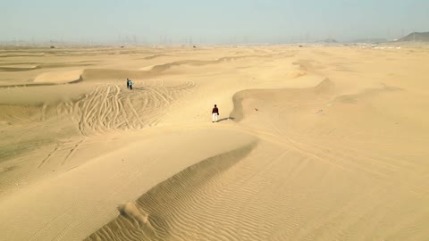 The soft golden sands, a drone shot of a Saudi Arabian Gulf Arab man walking in the desert in Mecca, Saudi Arabia.