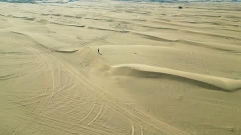 The soft golden sands, a drone shot of a Saudi Arabian Gulf Arab man walking in the desert in Mecca, Saudi Arabia.