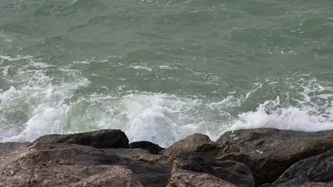 Sunset over the sea at Palm Jumeirah. Waves crashing rocks on the beach at Dubai Rocky Beach. Ocean waves crashing over mossy rocks at sunset with vibrant blue sky