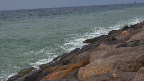 Sunset over the sea at Palm Jumeirah. Waves crashing rocks on the beach at Dubai Rocky Beach. Ocean waves crashing over mossy rocks at sunset with vibrant blue sky