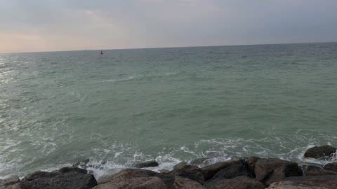 غروب الشمس فوق البحر في نخلة جميرا. أمواج تتلاطم على الصخور على شاطئ دبي الصخري. أمواج المحيط تتلاطم على الصخور المغطاة بالطحالب عند غروب الشمس مع سماء زرقاء صافية.