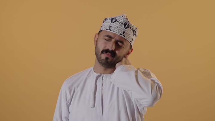آلام شديدة في الرقبة والعنق، ايماءات وجه تدل على الوهن الشديد، ألم في المفاصل، بورتريه مقرب لرجل عماني شايب يرتدي الدشداشة والكمه يشعر بالتعب و الارهاق، خلفية برتقالية