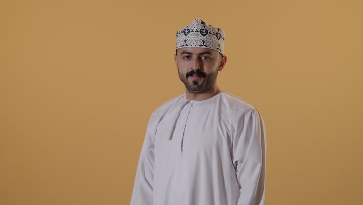 علامة الجودة والامتياز, بورتريه مقرب لرجل عربي خليجي عماني يرتدي الدشداشة و الكمة يرفع ابهامه بإيماءات الموافقة والقبول, الاعجاب والرضا لتحقيق أمر معين، خلفية برتقالية