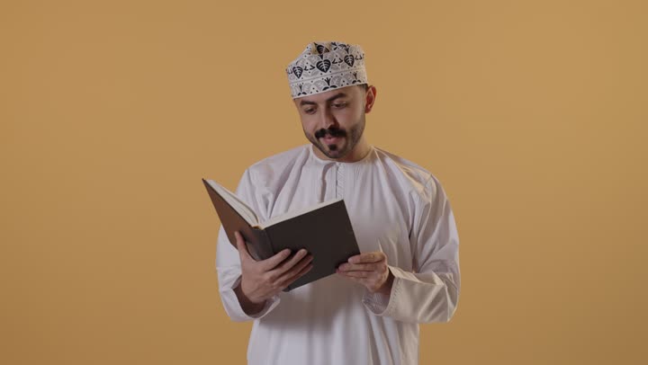 هواية القراءة والاستكشاف، قضاء وقت الفراغ بالتعلم والثقافة، مفهوم التثقيف والبحث العلمي، بورتريه لرجل عربي خليجي عماني يرتدي الدشداشة و الكمة يقرأ كتاب، خلفية برتقالية