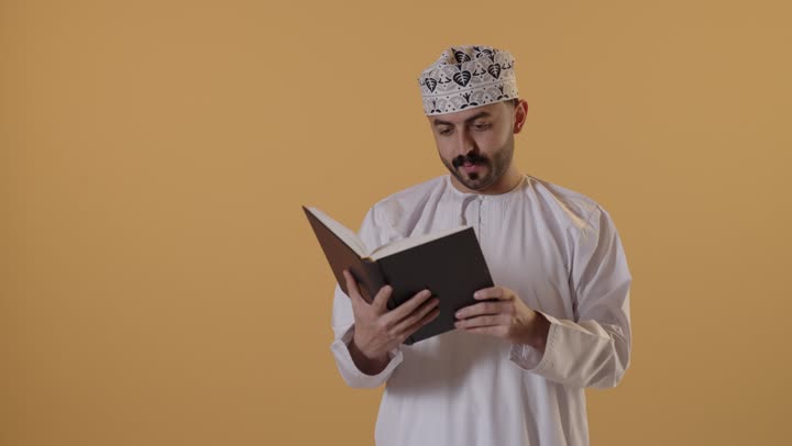 قضاء وقت الفراغ بالتعلم والثقافة، مفهوم التثقيف والبحث العلمي، بورتريه لرجل عربي خليجي عماني يرتدي الدشداشة و الكمة يقرأ كتاب, هواية القراءة والاستكشاف، خلفية برتقالية