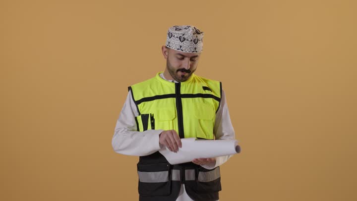 مفهوم الهندسة والانشاءات المعمارية، ايماءات الاندماج و التركيز، بورتريه  لمهندس عربي خليجي عماني يرتدي  الدشداشة و الكمة و سترة الحماية يمسك مخطط الإعمار يقوم بمتابعة الأعمال، مهن ووظائف شبابية، الإعمار بسواعد أبناء الوطن، خلفية برتقالية