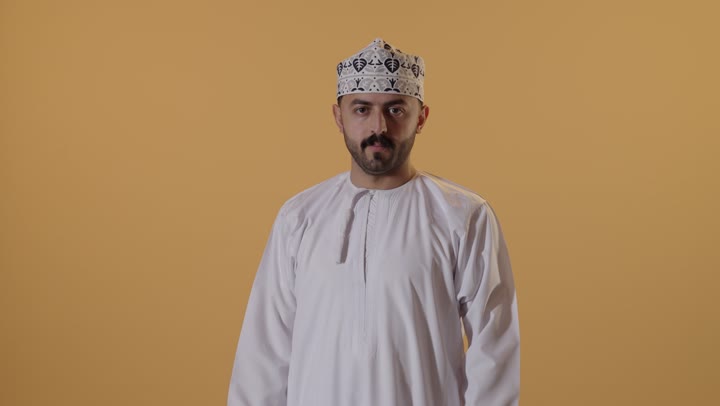 إستعراض القوة البدنية ، لياقة بدنية وصحة، بورتريه مقرب لرجل عربي خليجي عماني  يرتدي  الدشداشة و الكمة يرفع يده بكفه مقبوضه ، مفهوم القوة العضلية وعرض العضلات ، خلفية برتقالية