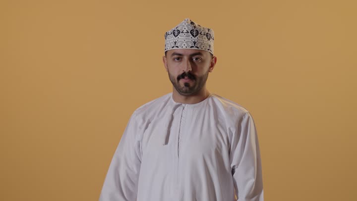 لياقة بدنية وصحة، إستعراض القوة البدنية ، بورتريه مقرب لرجل عربي خليجي عماني  يرتدي  الدشداشة و الكمة يرفع يده بكفه مقبوضه ، مفهوم القوة العضلية وعرض العضلات ، خلفية برتقالية