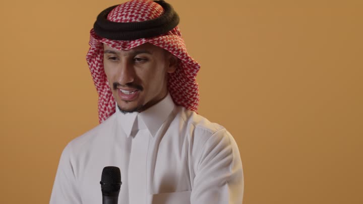 القاء الخطابات والكلمات باستخدام مكبر الصوت، القيام بالحوارات والنقاشات، تبادل الحوار والاستفادة من الخبرات، بورتريه مقرب لرجل عربي خليجي سعودي يرتدي الثوب الابيض و الشماغ يحمل بيده مكبر الصوت، خلفية برتقالية